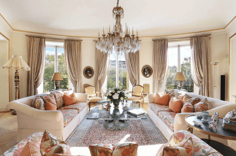 Grand salon parisien Haussmannien de luxe avec canapés floraux, chandelier en cristal, mobilier classique et vue sur parc.
