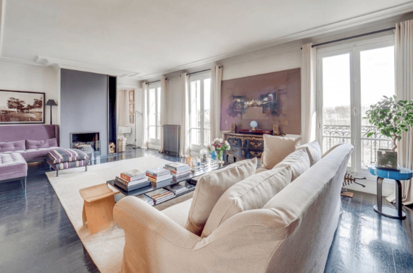 Salon moderne et élégant avec grand canapé crème, parquet sombre, cheminée contemporaine et canapé violet. Luminosité par grandes fenêtres.