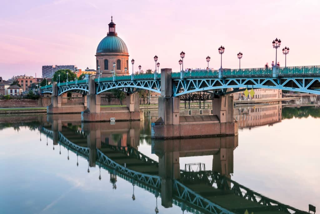 Pont Saint-Pierre et dôme de La Grave se reflètent dans la Garonne à Toulouse. Ciel rose crépusculaire, lampadaires et marqueur 'III'.